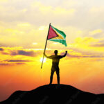 Guyana flag being waved by a man celebrating success at the top of a mountain against sunset or sunrise. Guyana flag for Independence Day.