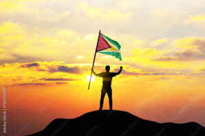 Guyana flag being waved by a man celebrating success at the top of a mountain against sunset or sunrise. Guyana flag for Independence Day.