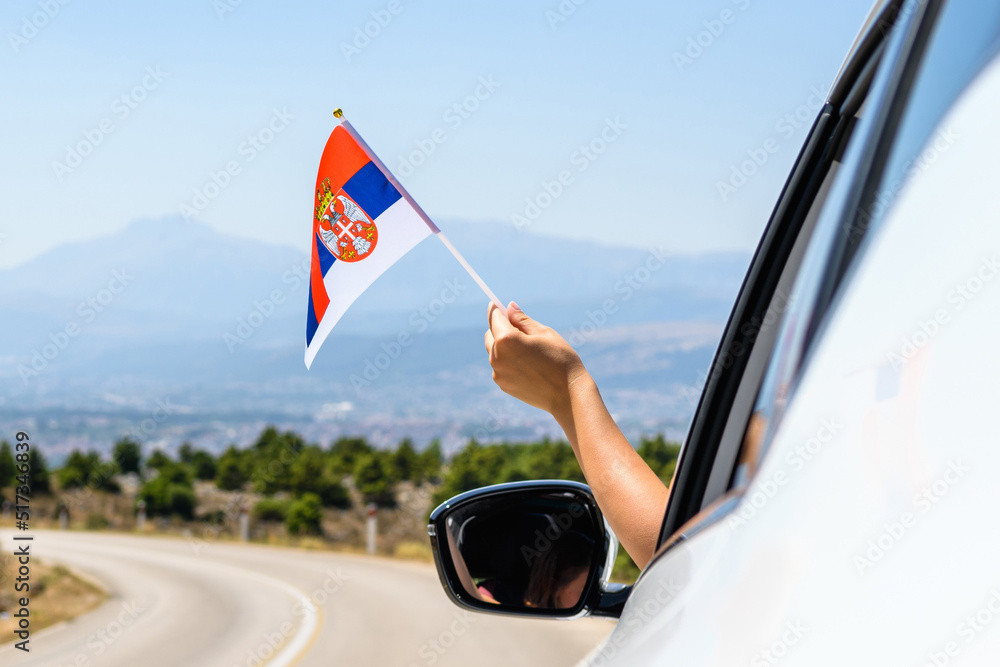 Woman holding Serbia flag from the open car window driving along the serpentine road in the mountains. Concept