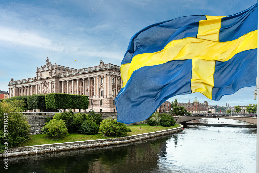 The building of the Swedish Parliament (Riksdag) and the Riksbank Bridge over the Lilla Vartan Strait with the national flag of Sweden in the foreground.